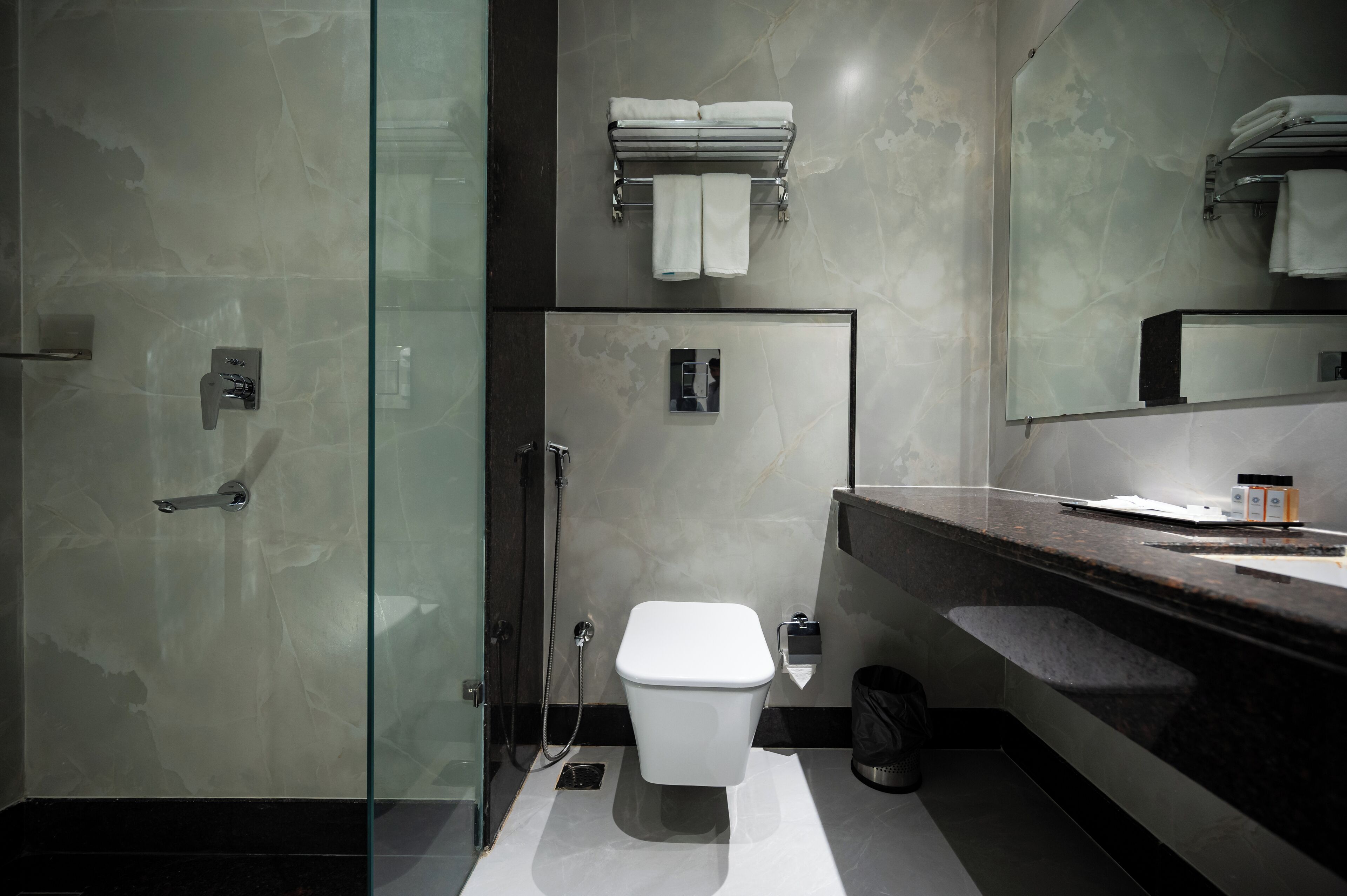 A modern bathroom with a glass shower enclosure, a white toilet, and a marble-tiled vanity.