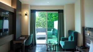 A modern hotel room with a glass door leading to a balcony, a flat-screen TV, a small table, and two chairs. - The Hotel Mudra (Varanasi)