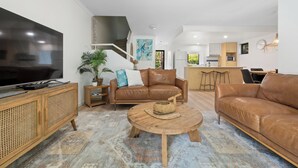 A modern living room with a large flat-screen TV, leather sofas, a wooden coffee table, and a patterned rug. - Unit 94 - Modern and Stylish 2 Bedroom Townhouse in Resort (Noosaville)