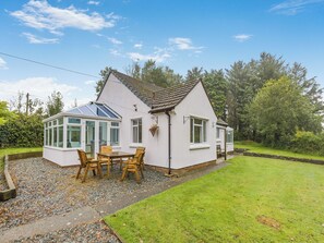 Une maison blanche avec une véranda, une terrasse dotée de meubles en bois et un jardin bien entretenu.