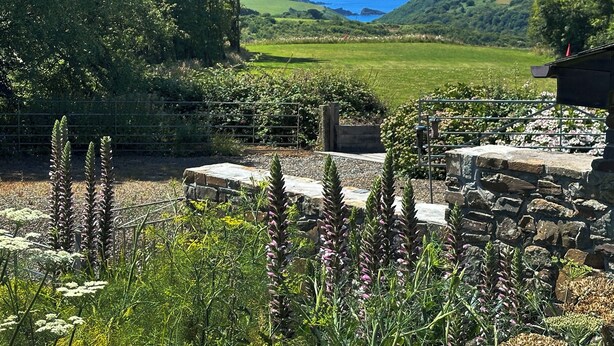 A garden with stone structures and a view of the sea. - Pine Cottage - UK46874 (Hartland)
