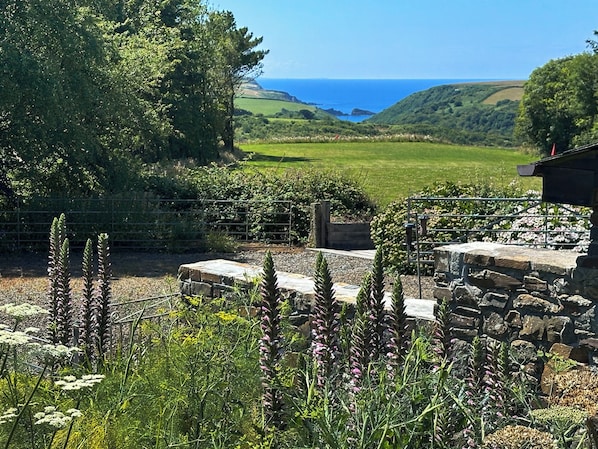 A garden with stone structures and a view of the sea.