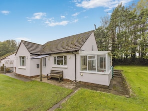 A white house with a tiled roof, a wooden bench, and a small garden.