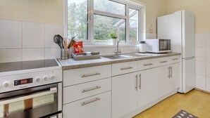 A kitchen with white cabinets, a stove, a microwave, and a window with a view of trees. - Pine Cottage - UK46874 (Hartland)
