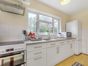 A kitchen with white cabinets, a stove, a microwave, and a window with a view of trees.