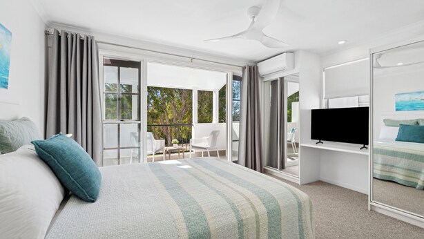 A modern hotel room with a large bed, a flat-screen TV, and a balcony with outdoor seating.