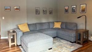 A modern living room with a grey sectional sofa, a small wooden side table, a floor lamp, and a patterned rug.
