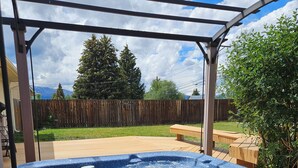 A hot tub under a covered patio with a wooden fence and trees in the background.