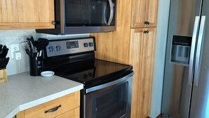 A kitchen with wooden cabinets, a stainless steel refrigerator, a microwave, and a stove.