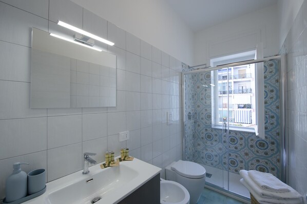 A bathroom with a white sink, mirror, and toilet. There is a window with a view of a balcony. - Suite Positano - 100 meters from the beach (Maiori)