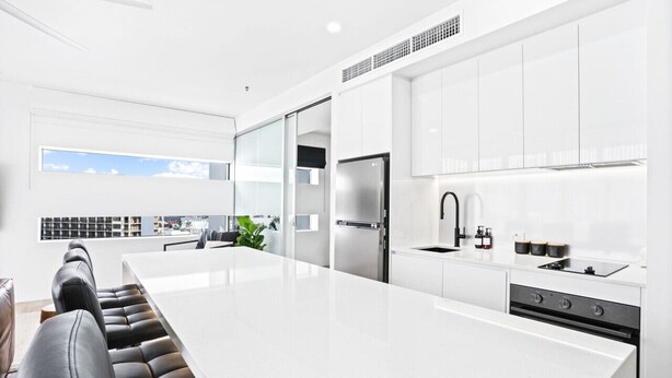 Une cuisine moderne avec des meubles blancs, un grand îlot central et un coin repas doté de chaises en cuir noir.