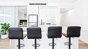 Une cuisine moderne avec des meubles blancs, un îlot central doté de tabourets et un réfrigérateur visible.