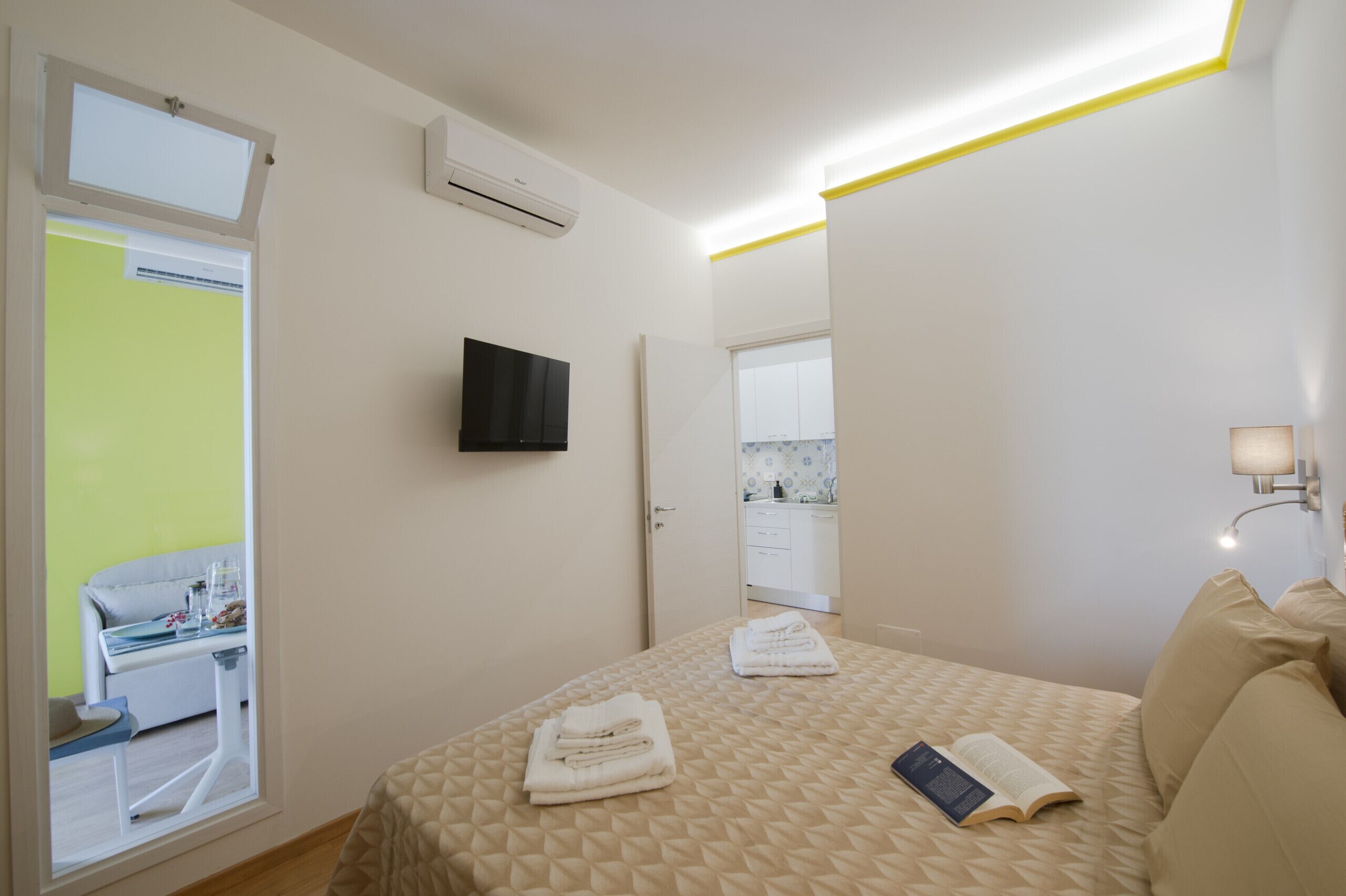 Una camera d'hotel con un letto, una televisione, una finestra e un bagno visibile attraverso una porta aperta.