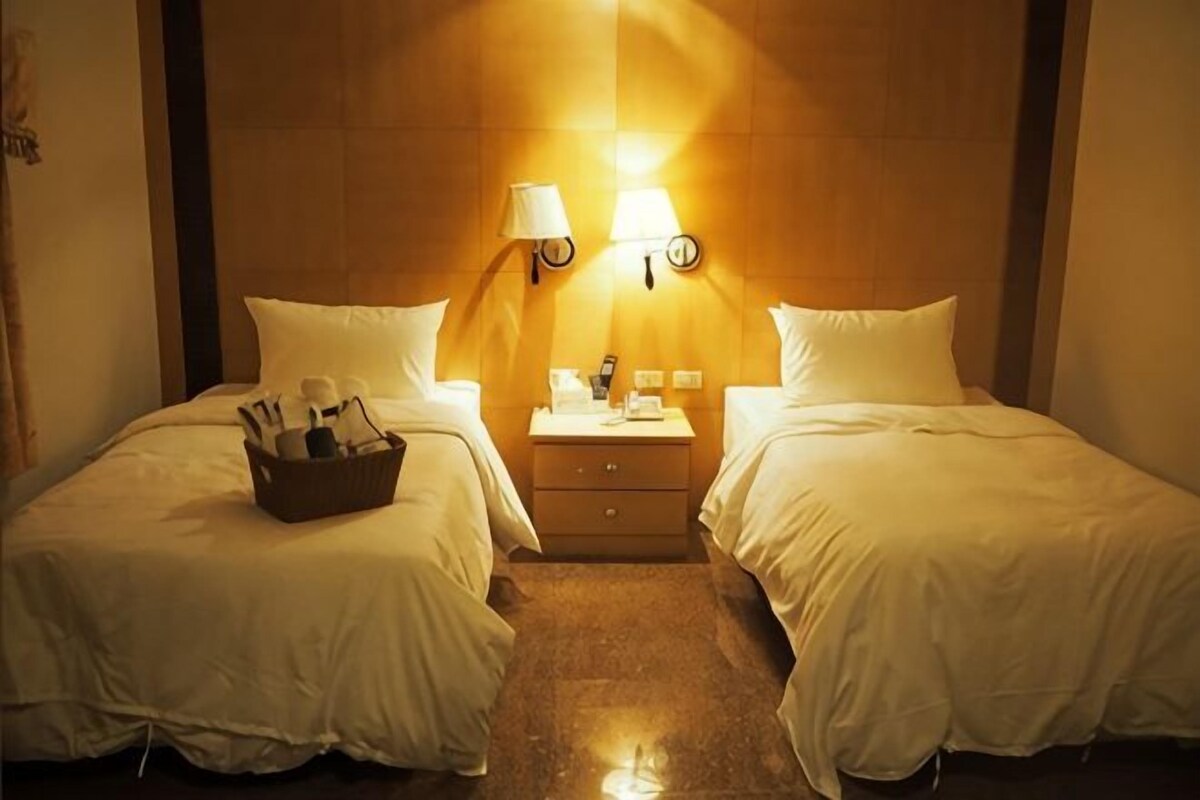 A hotel room with two beds, a nightstand with a lamp, and a small table with a lamp.