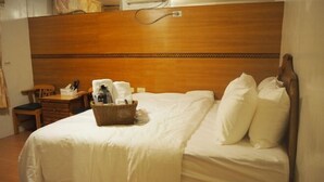 A hotel room with a wooden headboard, a neatly made bed with white linens, a small wooden nightstand with a lamp, and a wicker basket on the bed. - Shexia Li Yu (Pingtung)