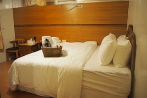 A hotel room with a wooden headboard, a neatly made bed with white linens, a small wooden nightstand with a lamp, and a wicker basket on the bed. - Shexia Li Yu (Pingtung)