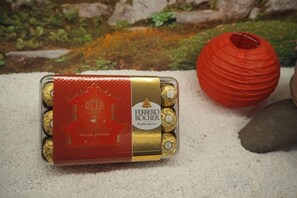 A Ferrero Rocher chocolate box on a textured surface with a red spherical object nearby.