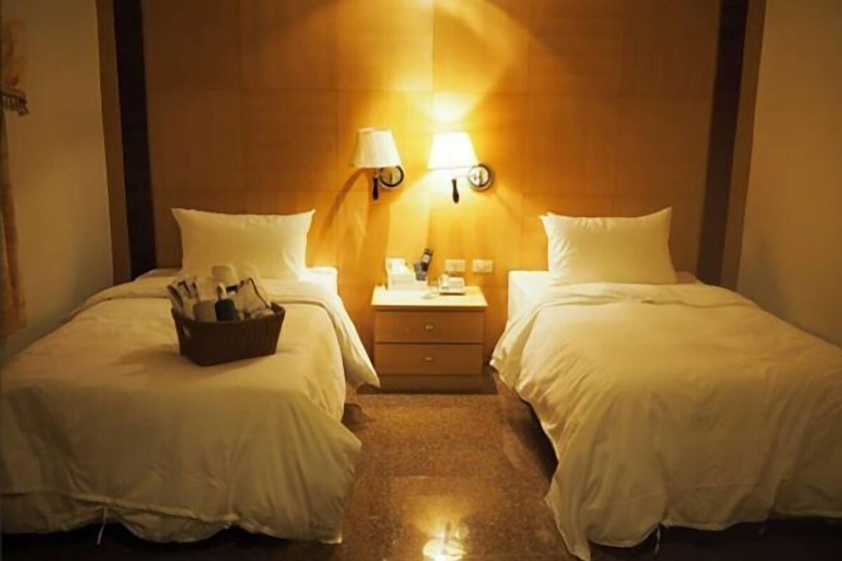 A hotel room with two beds, a nightstand, a lamp, and a small table.