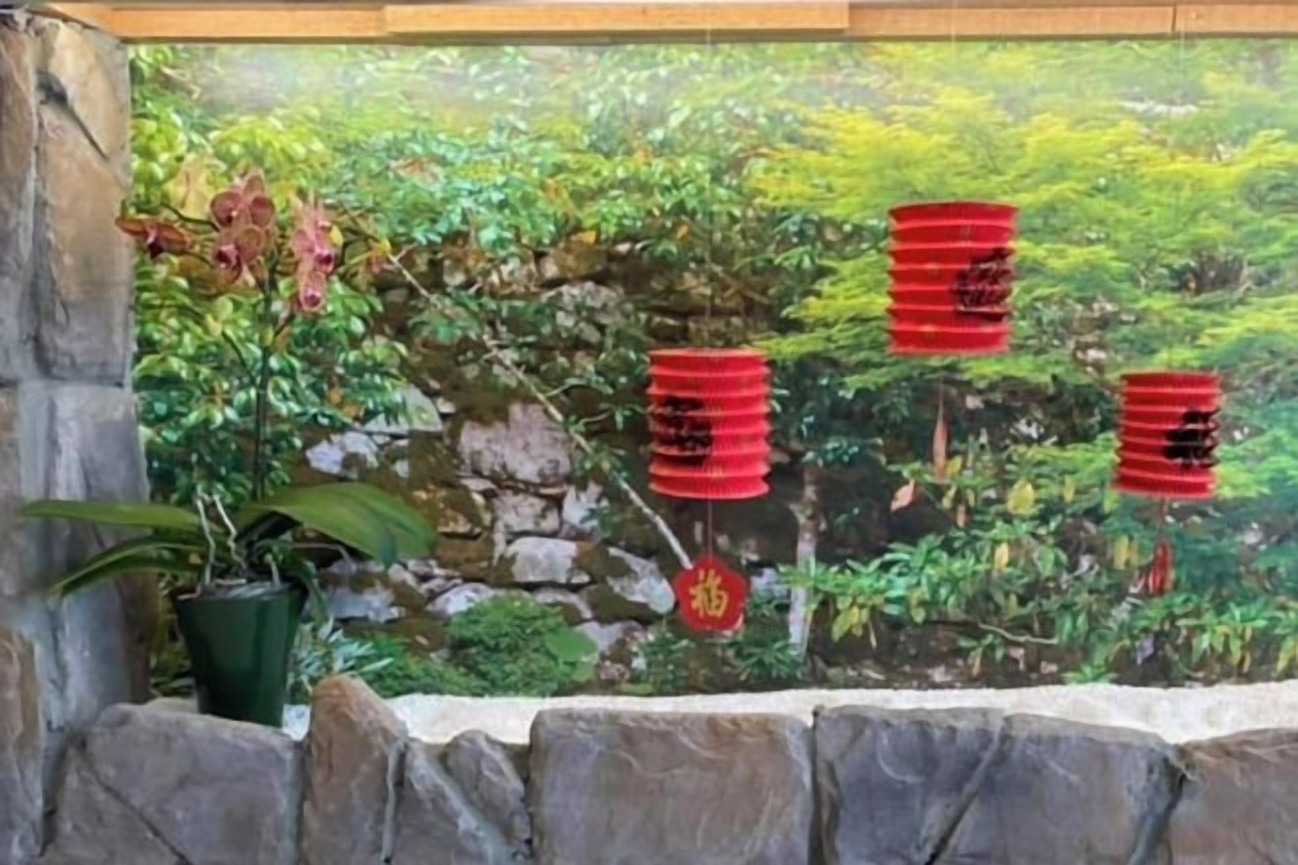 Parede de pedra com um mural de vegetação e lanternas vermelhas.