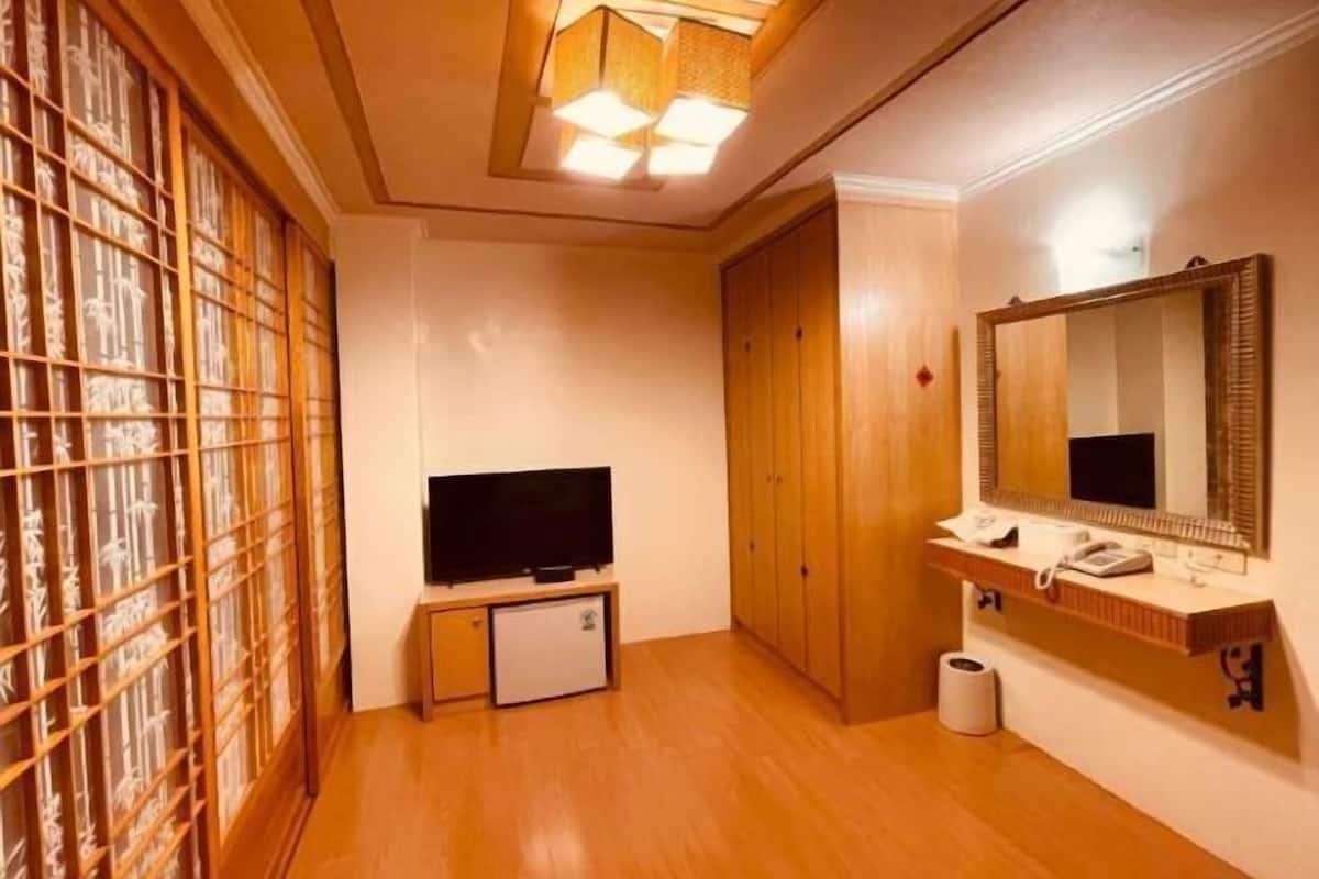 A room with a television, a small refrigerator, a wooden wardrobe, a mirror, and a toilet.