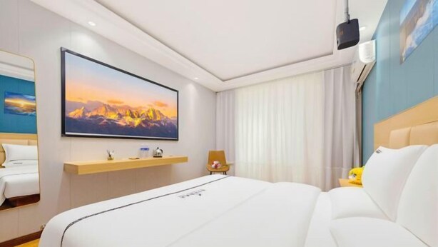 Ett hotellrum med en stor säng, en TV som hänger på väggen, ett skrivbord med en stol och ett fönster med gardiner.