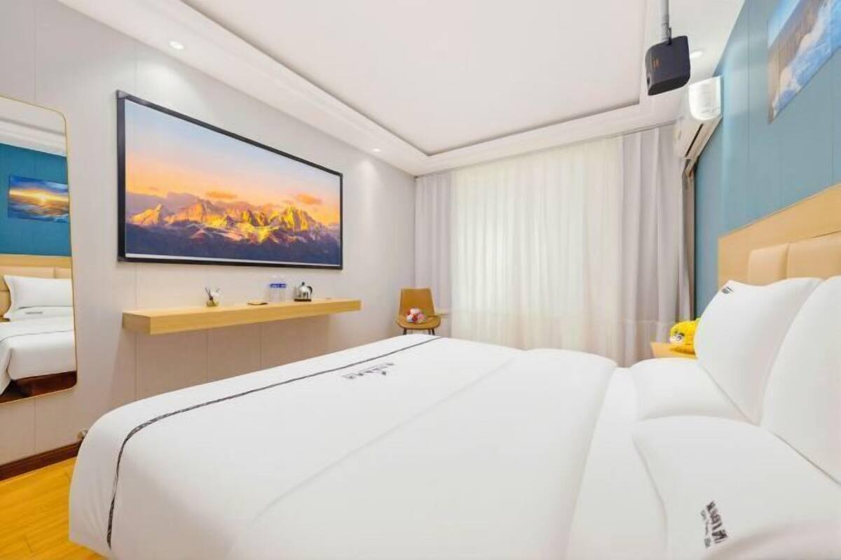 Ein Hotelzimmer mit einem großen Bett, einem Wand-Fernseher, einem Schreibtisch mit Stuhl und einem Vorhangfenster.