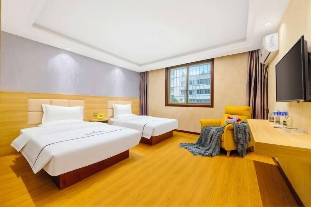 Ein Hotelzimmer mit zwei Betten, einem Schreibtisch, einem Stuhl, einem Fernseher und einem Fenster.