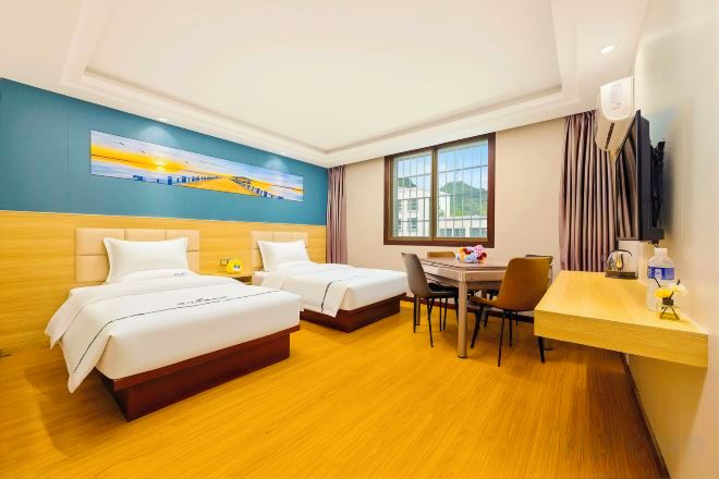 Habitación de hotel con dos camas, un escritorio, una silla, un televisor y una ventana con cortinas.