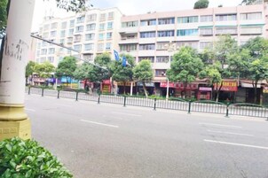 Una calle con edificios de varios pisos, una cerca peatonal y árboles.