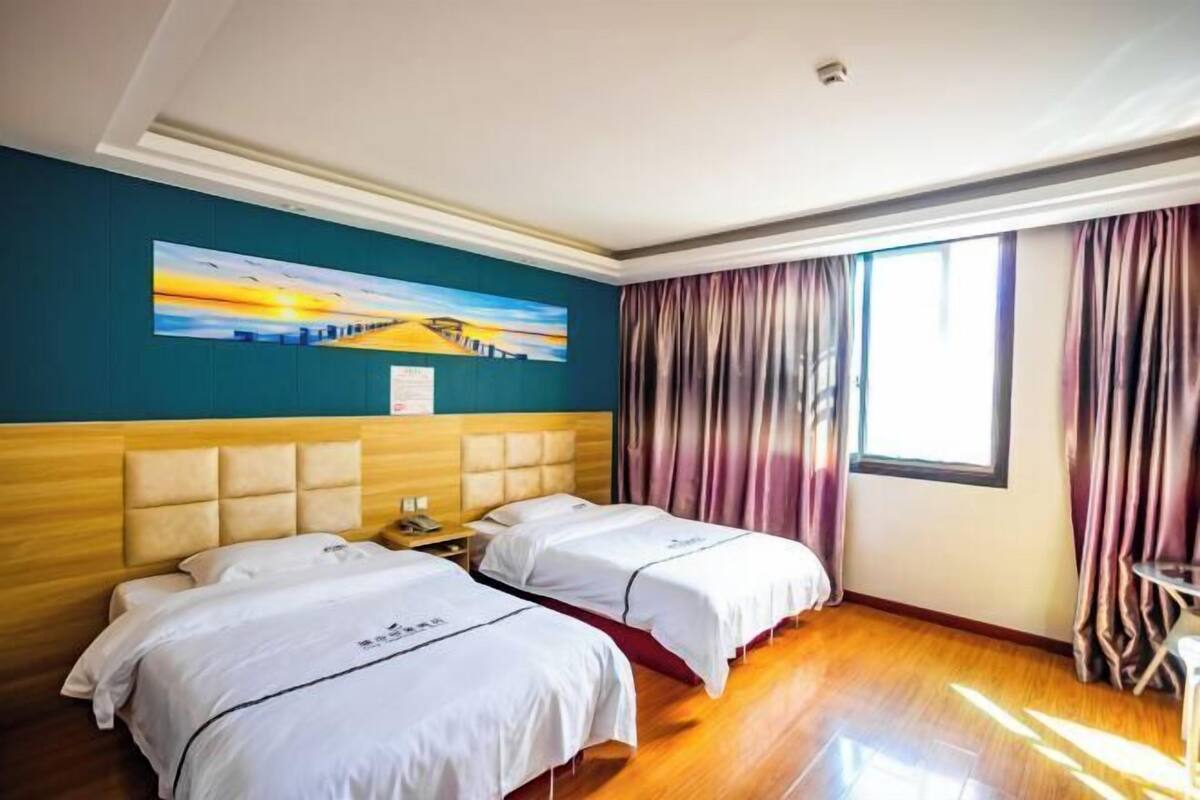 Ein Hotelzimmer mit zwei Betten, einem Bild an der Wand, einem Fenster mit Vorhängen und Holzboden.