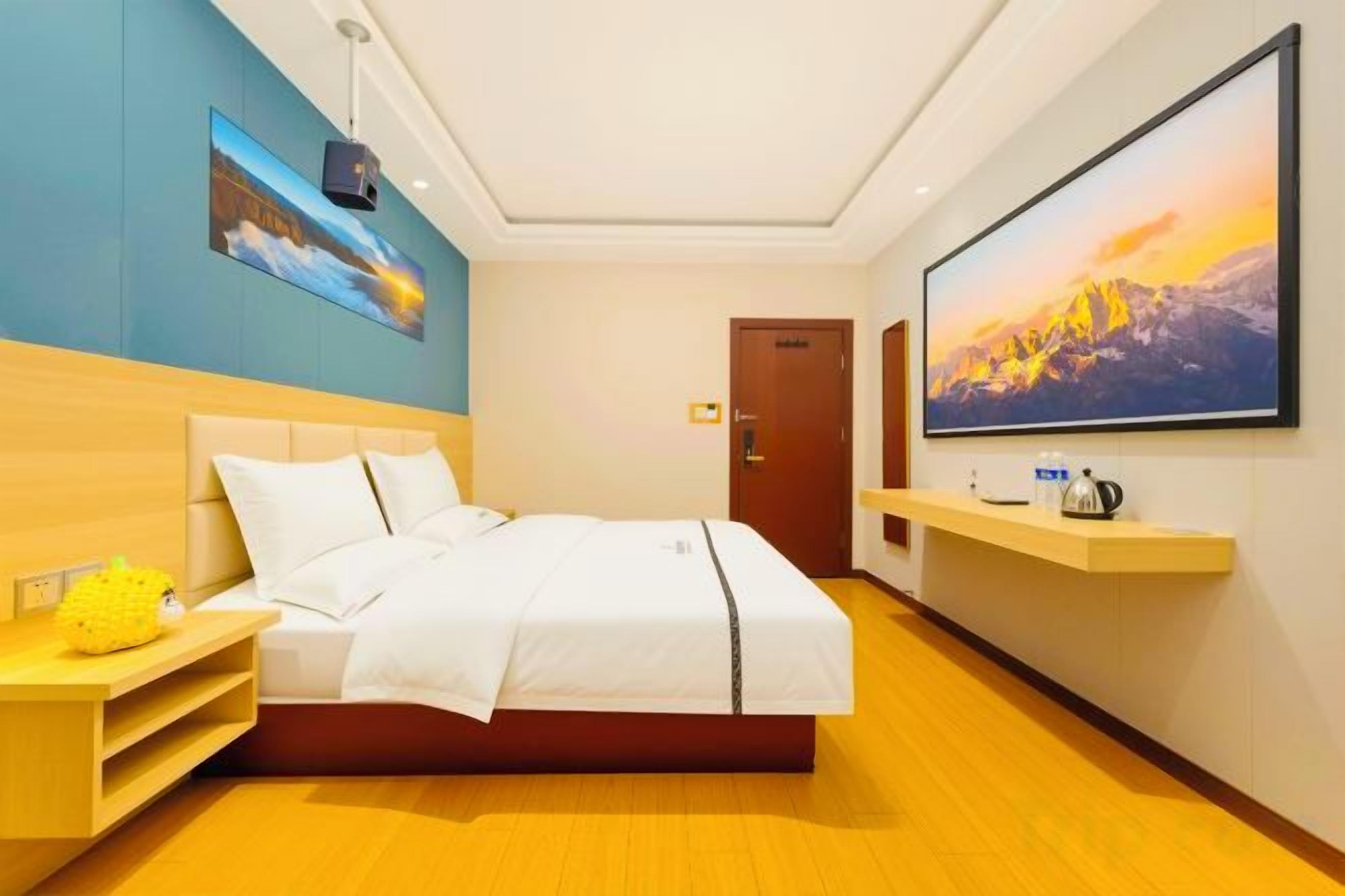 Habitación de hotel con una cama, un televisor montado en la pared, una mesita de noche de madera y un cuadro sobre la cama.