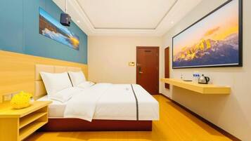A hotel room with a bed, a TV mounted on the wall, a wooden nightstand, and a painting above the bed.