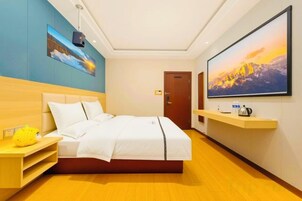 Habitación de hotel con una cama, un televisor montado en la pared, una mesita de noche de madera y un cuadro sobre la cama.
