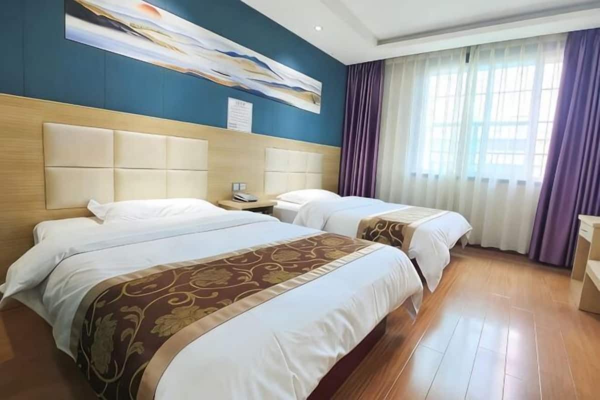 Ein Hotelzimmer mit zwei Betten, einem Holzkopfstück, einem großen Gemälde an der Wand und einem Fenster mit Vorhängen.