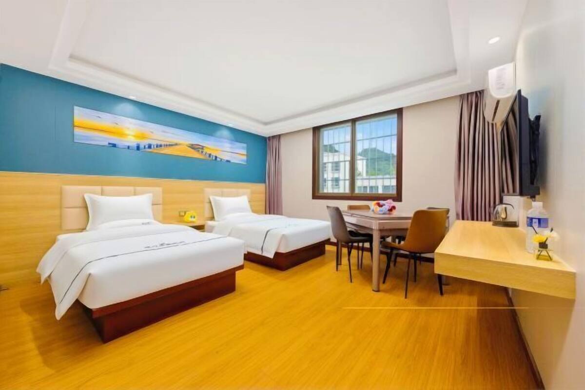 Ein Hotelzimmer mit zwei Betten, einem Schreibtisch, einem Stuhl, einem Fenster und einem Bild an der Wand.