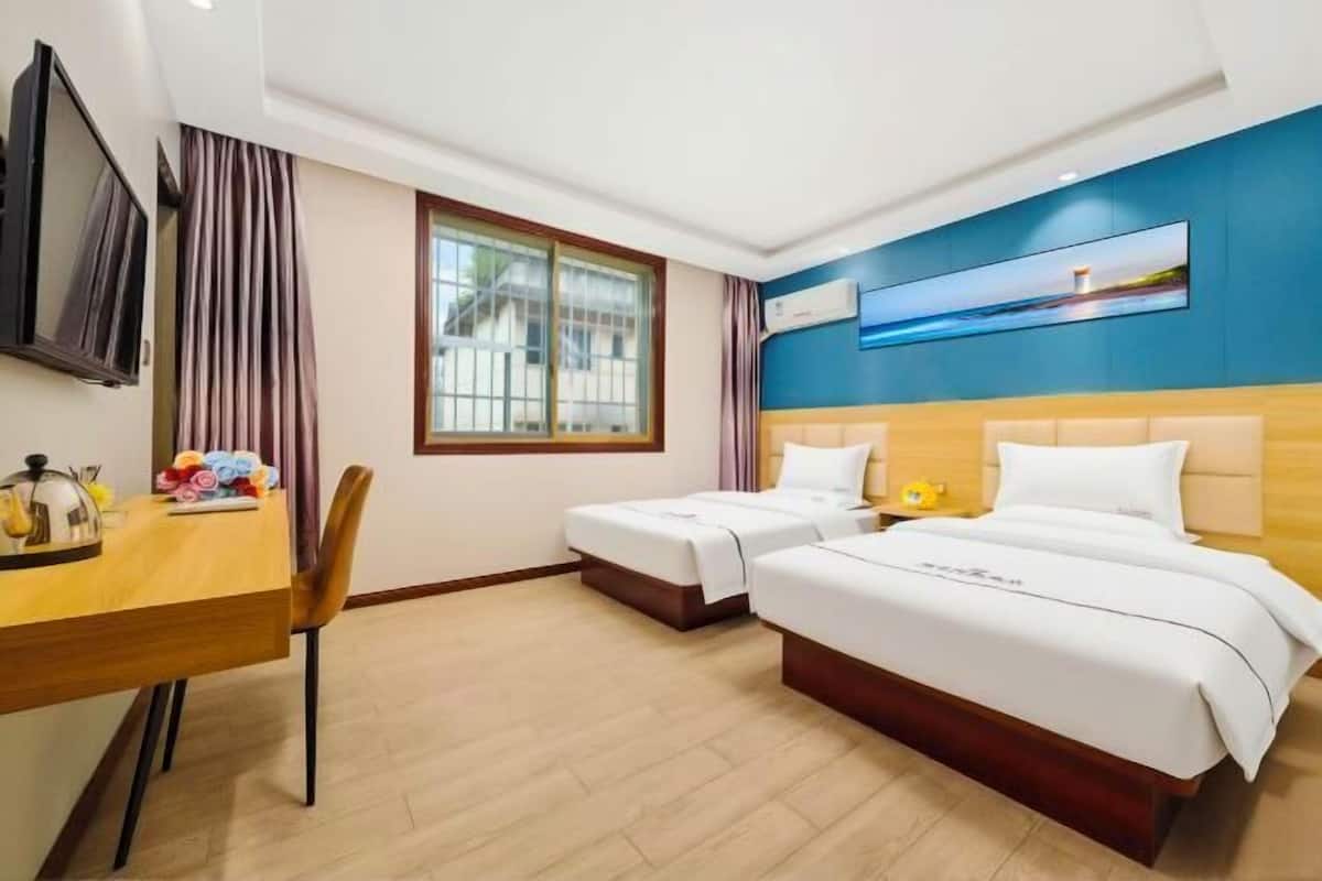 Ein Hotelzimmer mit zwei Betten, einem Schreibtisch, einem Fernseher und einem Fenster mit Vorhängen.