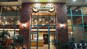 The exterior of a restaurant named "Vandalo" with a brick facade, large windows, and potted plants in front. - Rosetum Anjuna Goa (Anjuna)