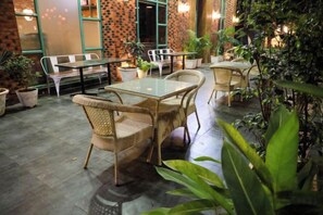 An outdoor seating area with wicker chairs and tables, surrounded by potted plants and a brick wall. - Rosetum Anjuna Goa (Anjuna)