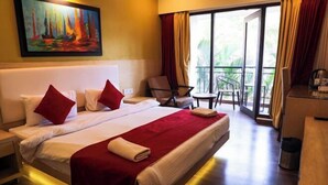 A hotel room with a large bed, a painting on the wall, a balcony with chairs, and a desk. - Rosetum Anjuna Goa (Anjuna)
