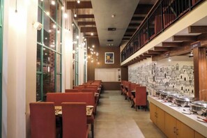 A restaurant with long tables and chairs, a counter with dishes, and a wall with drawings. - Rosetum Anjuna Goa (Anjuna)