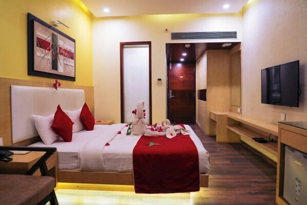 A hotel room with a bed, bedside table, TV, and a red decorative item on the bed. - Rosetum Anjuna Goa (Anjuna)