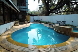 A swimming pool with a curved edge, surrounded by a white wall and a wooden deck. - Rosetum Anjuna Goa (Anjuna)