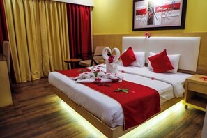A hotel room with two beds, red and white bedding, a wooden floor, and a red curtain. - Rosetum Anjuna Goa (Anjuna)