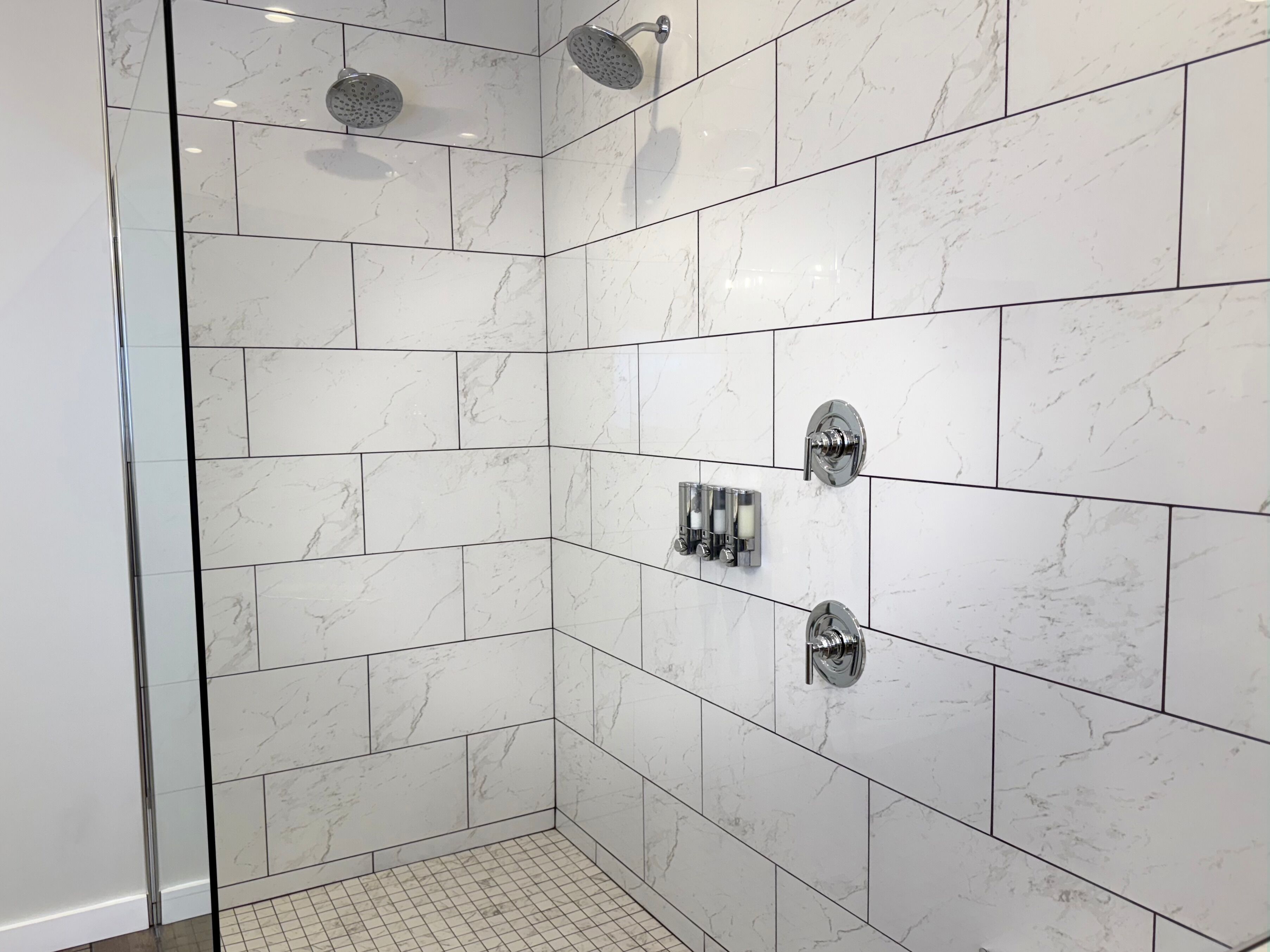 A modern shower with white marble tiles and chrome fixtures.