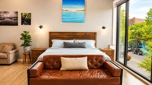 Un dormitorio con una cama grande, un sofá de cuero, una planta en maceta y obras de arte en las paredes.