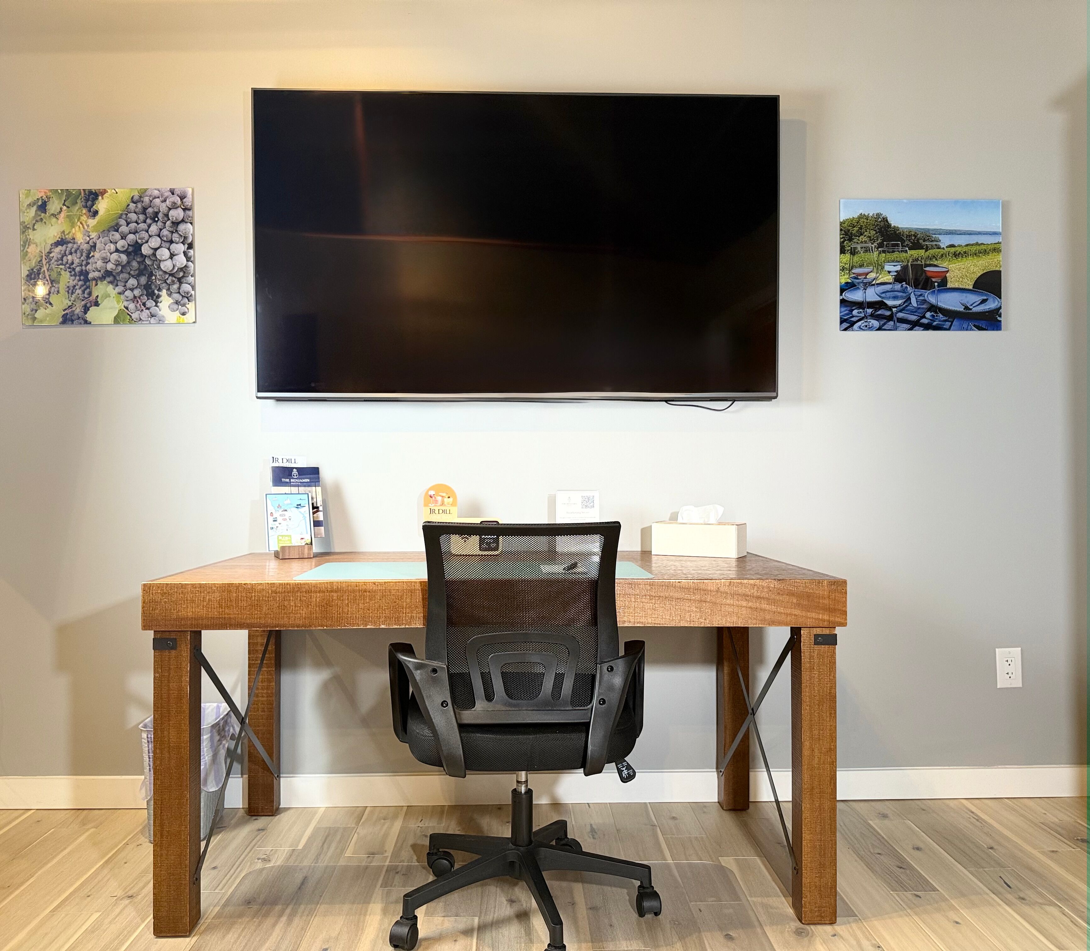 Una habitación con un televisor de pantalla plana grande montado en la pared, un escritorio de madera con una silla de oficina negra y dos cuadros enmarcados.