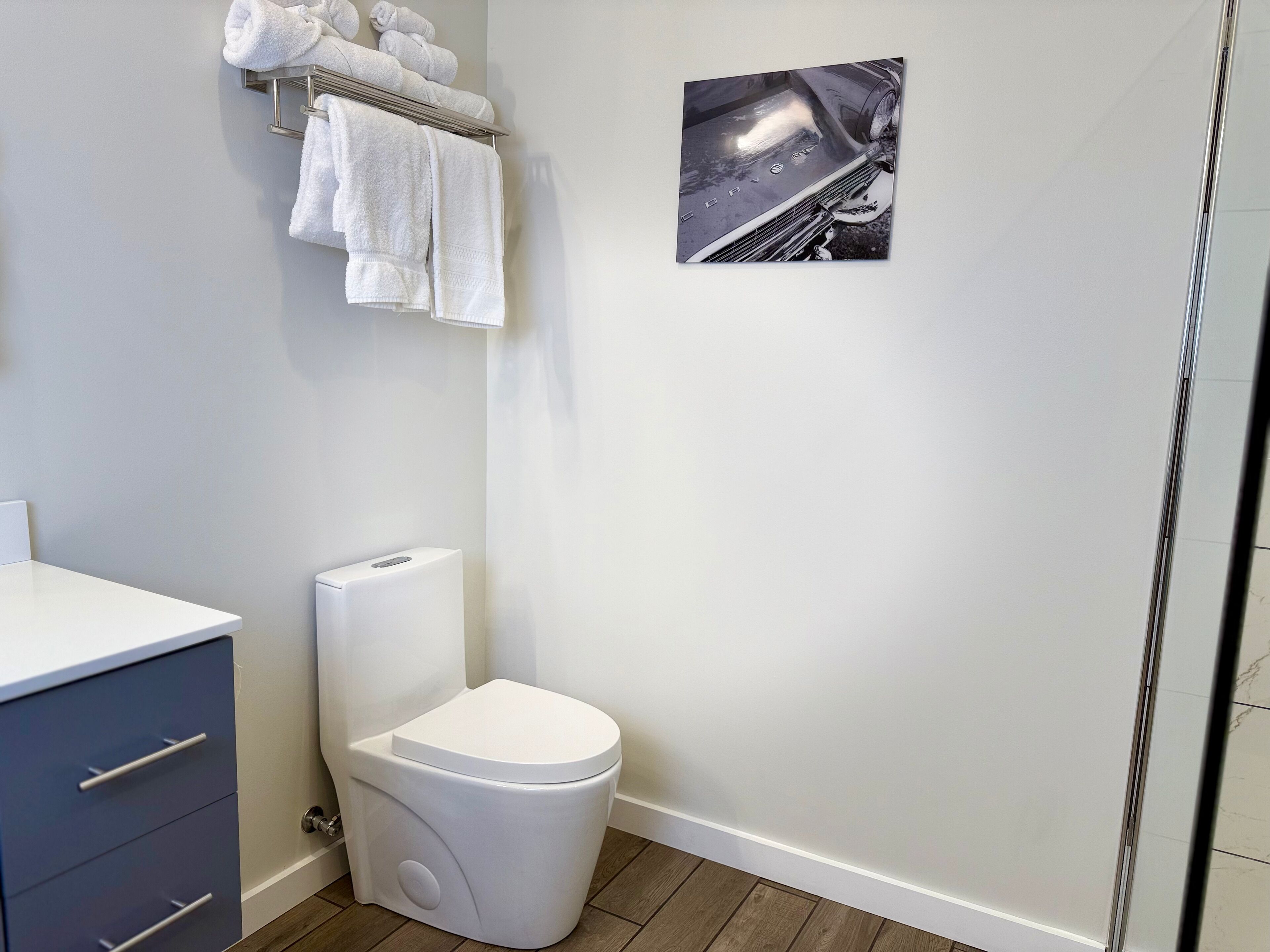 A modern bathroom with a white toilet, a towel rack with neatly folded towels, and a framed picture on the wall.