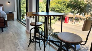Un interior moderno con suelo de madera, una mesa redonda con una silla y vistas a una calle con edificios y árboles.