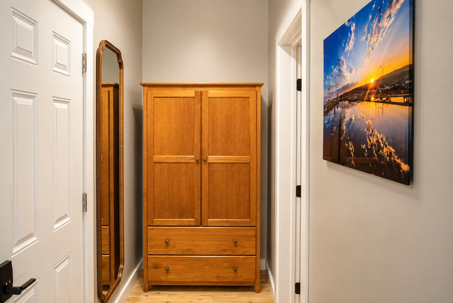 A hallway with a wooden wardrobe, a full-length mirror, and a framed picture on the wall.