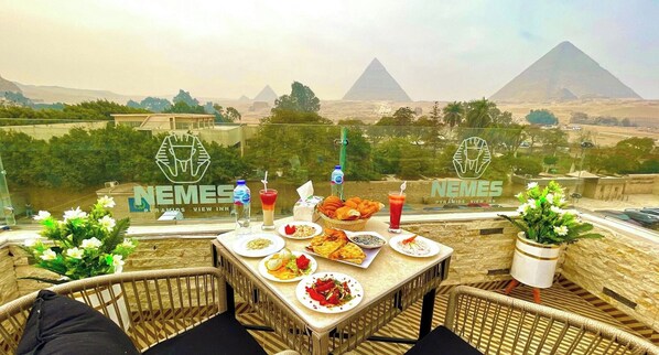 A table set with food and drinks, overlooking pyramids. - Nemes Pyramids View Inn (Giza)